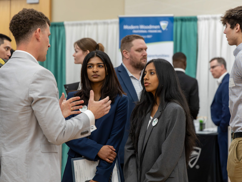 Two female students speaking a company representative during a career fair.