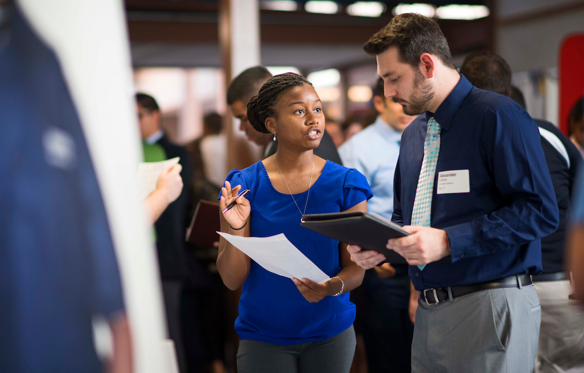 Photo of a career fair with a student and employer discussing a resume.